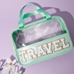 Mint green PVC and PU travel makeup bag with TRAVEL embroidery on light purple surface