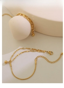 Detail of gold double-layered bracelet with snake chain, flat links and ball pendant