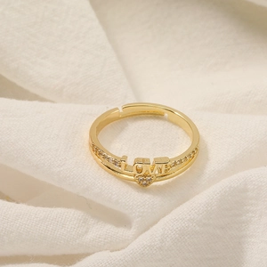 Detail of gold LOVE ring with micro-set zircon heart on white fabric background