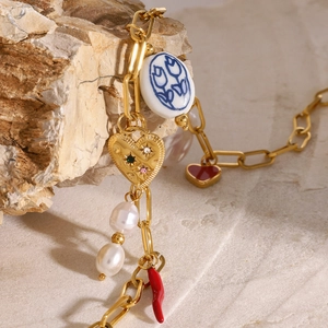 Gold necklace with pearl heart and chili charms displayed on a natural stone surface