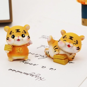 Macro shot of cute resin tiger figurines with gold fortune symbols and ingots on a desk