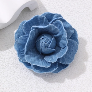 Macro detail of blue denim camellia brooch showing textured fabric petals and frayed edges