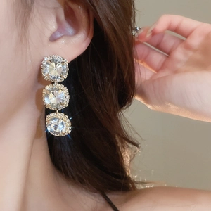 Close-up of model wearing elegant gold earrings with three cascading round rhinestones