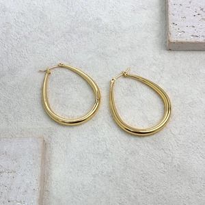 Minimalist gold teardrop hoop earrings with polished finish on a textured stone surface