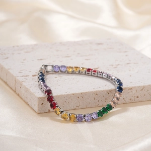 Close-up of a silver pavé bracelet with colorful faceted gemstones on textured beige stone