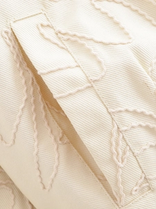 Vue macro d'une veste en toile crème avec broderie décorative en corde épaisse sur le bord