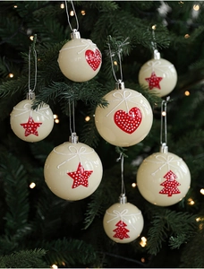 Close-up of white Christmas ornaments with red heart and star patterns on a tree