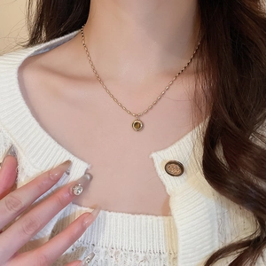 Close-up of a gold necklace with a round tiger eye stone pendant on a white cardigan