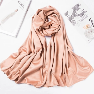 Detail of pink satin silk scarf showing smooth fabric texture and glossy finish on a plain surface