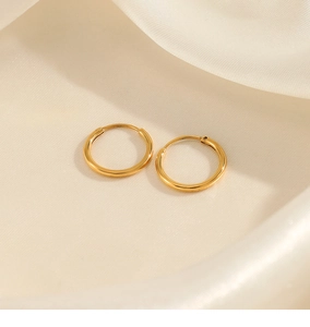 Macro shot of minimalist gold hoop earrings with smooth metallic finish on silk fabric