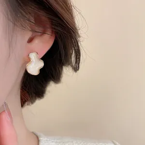 Gros plan d'une boucle d'oreille ondulée crème avec bord doré et fini nacré sur le mannequin