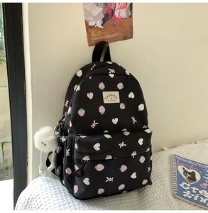 Close-up of black backpack featuring cute strawberry prints and a white fuzzy pompom charm