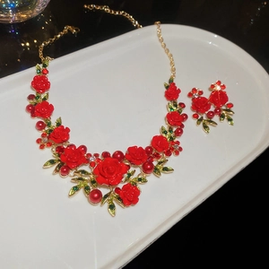 Close-up of red rose jewelry set with gold leaves and pearls on a white tray