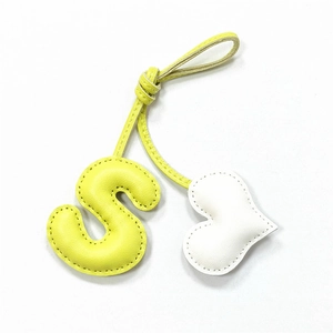 Detail of hand-stitched leather bag charm with yellow S letter and white heart pendant