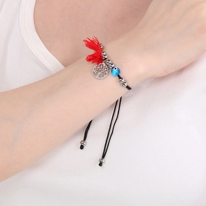 Close-up of woven bracelet featuring evil eye bead and tree of life charm on wrist