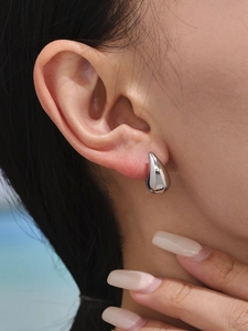 Macro view of water drop earrings in silver mirror finish worn on model ear