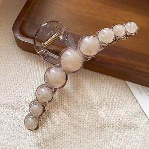 Detail of amber resin hair claw clip with faux pearl beads on a wooden tray