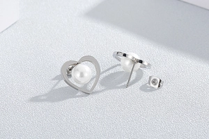 Macro shot of silver heart stud earrings with inlaid white pearls and metal backs