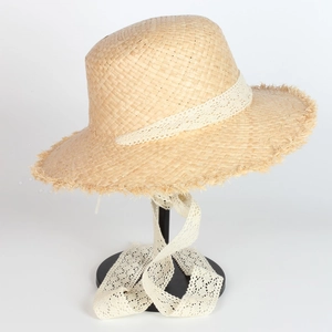 Detail of raffia sun hat featuring white lace ribbon and natural frayed edge brim