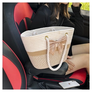 Detail of hand-woven straw tote bag with large champagne satin bow on car seat