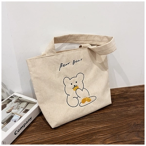 Close-up of beige corduroy tote bag with embroidered bear pattern on wooden table