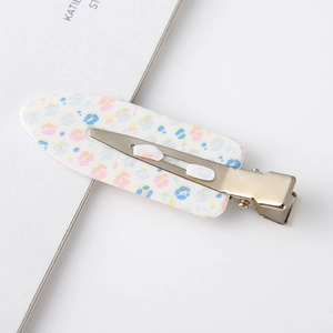 Macro detail of leaf-shaped hair clip with floral pattern and silver metal duckbill base
