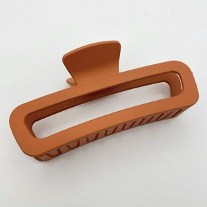 Detail of burnt orange matte square claw clip with hollow design and teeth on fabric