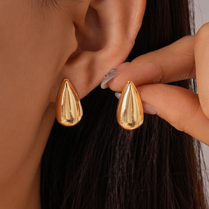 Gros plan de boucles d'oreilles gouttes dorées avec finition miroir tenues à la main