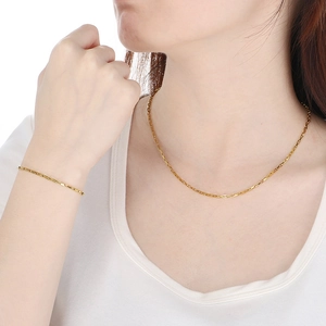 Close-up of golden box chain necklace and bracelet set worn by a model in white dress