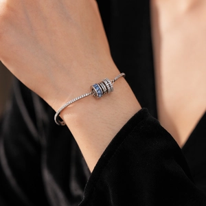 Close-up of silver bracelet with blue zircon pendant and Love Is A engraving