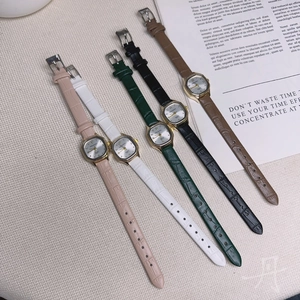 Square analog watches with leather straps in multiple colors on a cream fabric base