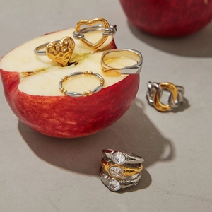 Close-up of gold and silver heart zircon rings displayed on a fresh red apple slice