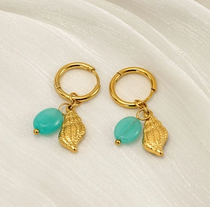 Detail of gold hoop earrings with turquoise beads and engraved seashell charms on silk