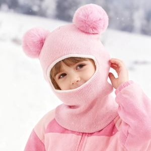 Detail of pink knitted baby balaclava with dual fur pom-poms on a snowy background
