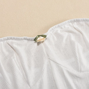 Detail of white ribbed knit dress featuring a beige fabric rose and green leaf accent