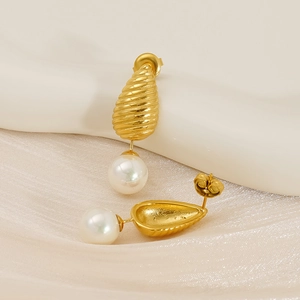 Vue détaillée de boucles d'oreilles goutte dorées texturées avec perles sur tissu soyeux