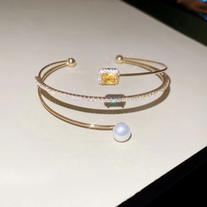 Detail view of gold floral bangle featuring yellow gemstone, pave diamonds and a white pearl