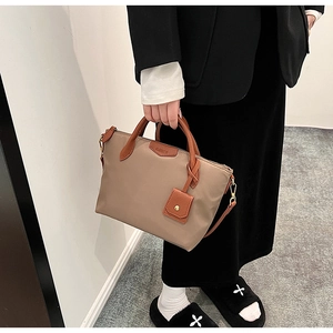 Detail view of khaki nylon tote bag with brown leather handles and brand charm