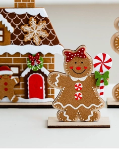 Detailed felt gingerbread man figurine with wooden base and festive Christmas house background