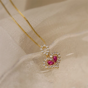 Close-up of golden heart pendant necklace with red pear-shaped stones on fabric