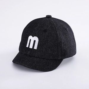 Detailed view of baby denim baseball cap with white embroidered letter M on black fabric