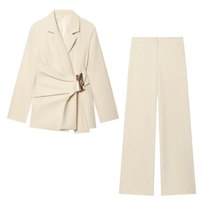 Detailed view of the irregular pleats and gold buckle on the cream blazer set