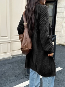 Vista posteriore di un cardigan nero in maglia a media lunghezza con texture e borsa in pelle marrone