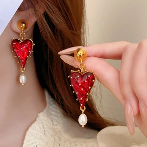 Detail of red tassel heart earrings with white pearls and gold metal on a model