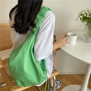Dettaglio della borsa hobo in nylon verde con tracolla a pieghe indossata da modella
