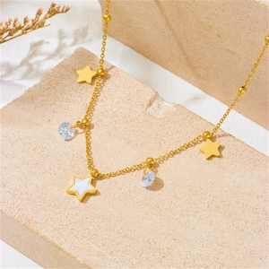 Gold stainless steel necklace with star and clear gem pendants on a beige stone surface