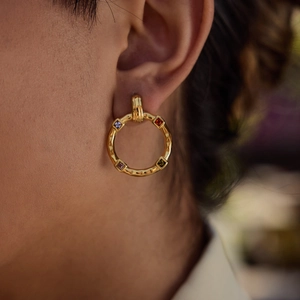 Hammered gold hoop earrings with multi-colored square gemstones worn on ear