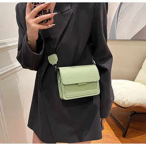 Close-up of a light green leather crossbody bag with a wide black fabric shoulder strap