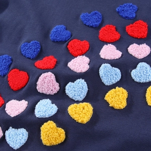 Detailaufnahme bunter Herz-Chenille-Stickereien auf dunkelblauem Mädchenkleidstoff