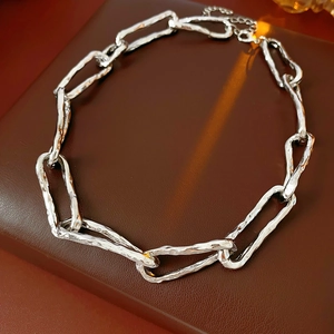 Detail shot of silver crinkled chain necklace on brown leather surface with warm lighting